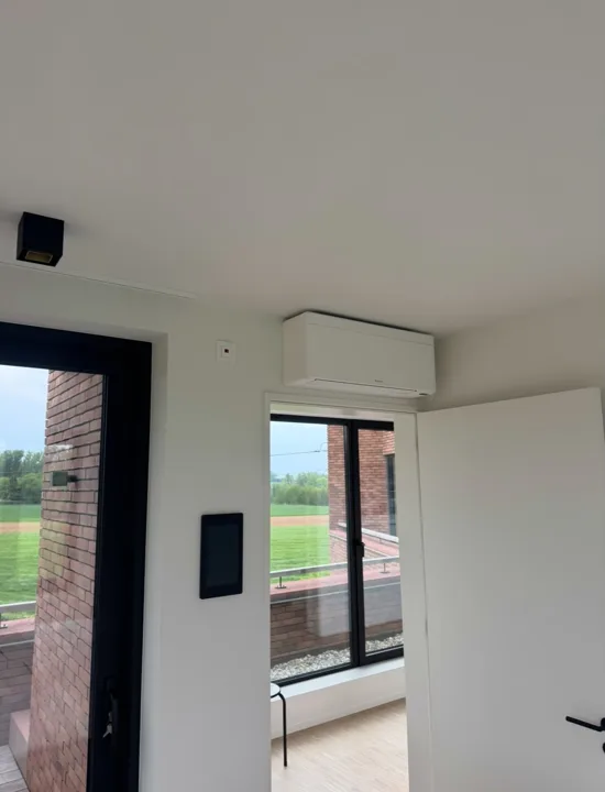 Witte airco boven een deuropening naast een zwart raamkozijn