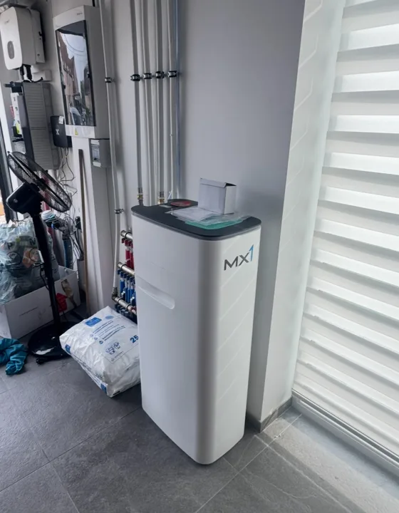 Witte waterverzachter naast leidingen in een technische ruimte